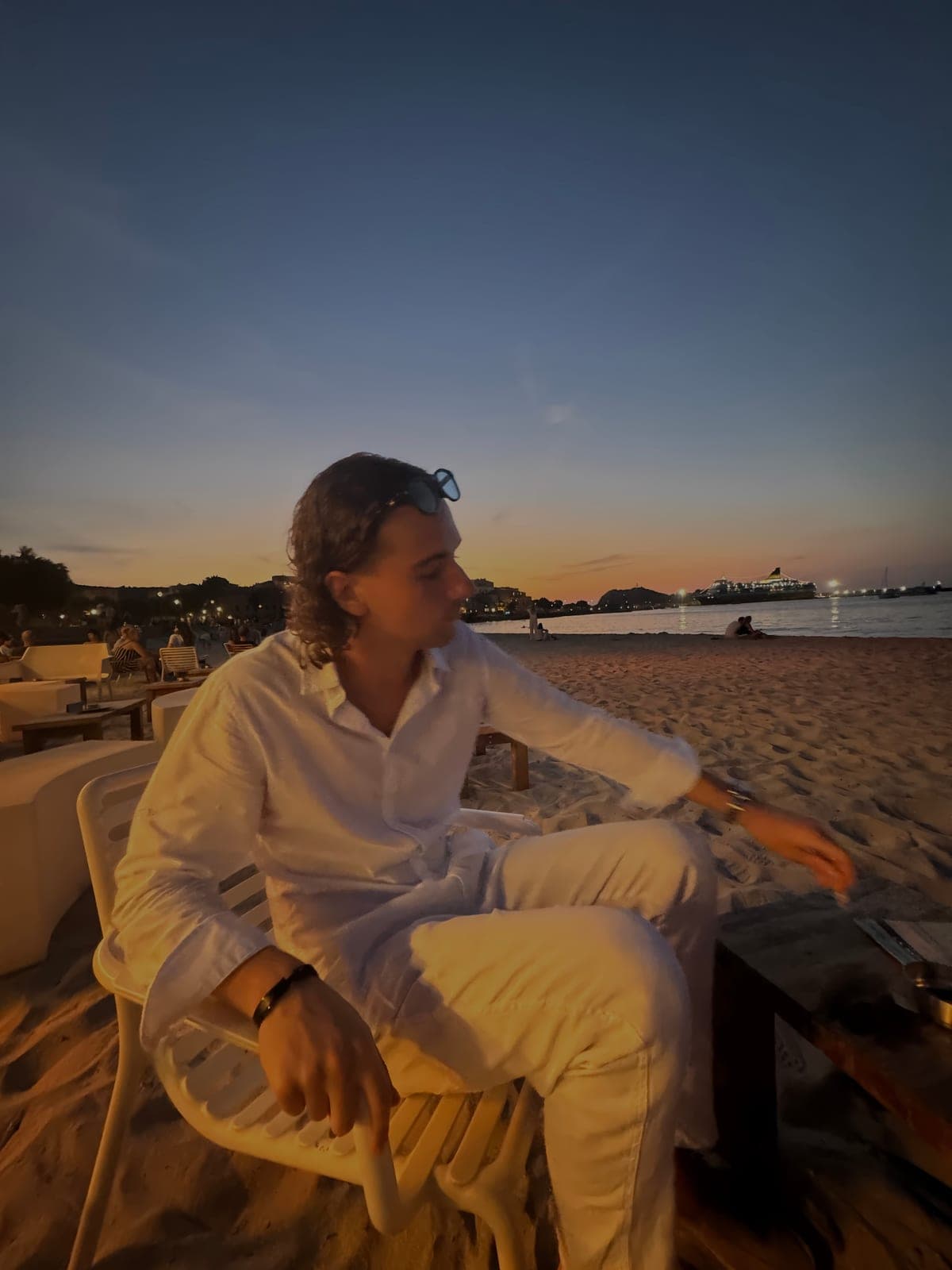Luka in a white outfit sitting on a beach at sunset