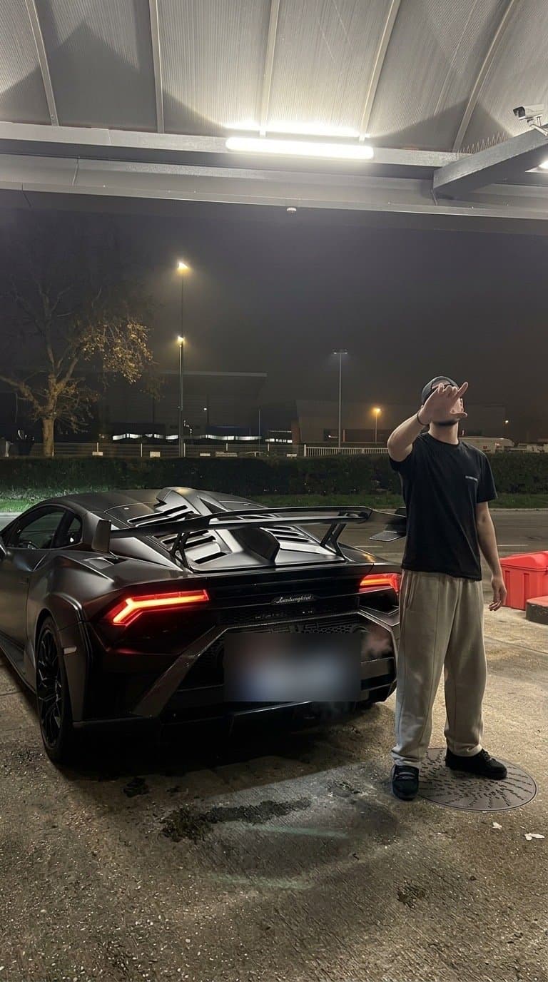 Luka standing next to the rear of his Lamborghini at night, taillights on