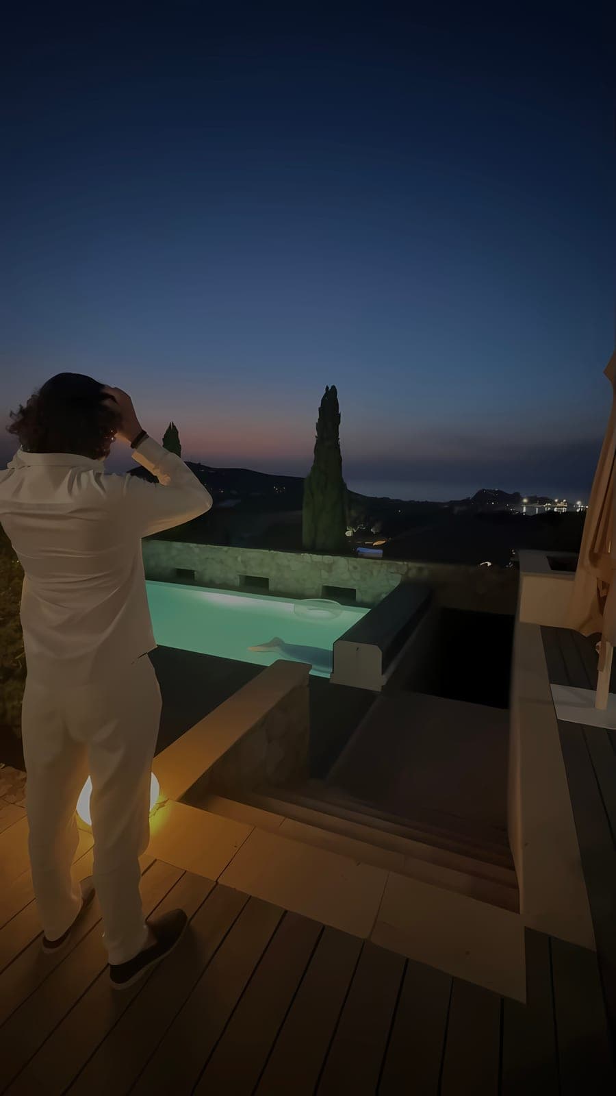 Luka at dusk on a villa terrace overlooking an illuminated pool and the coastline